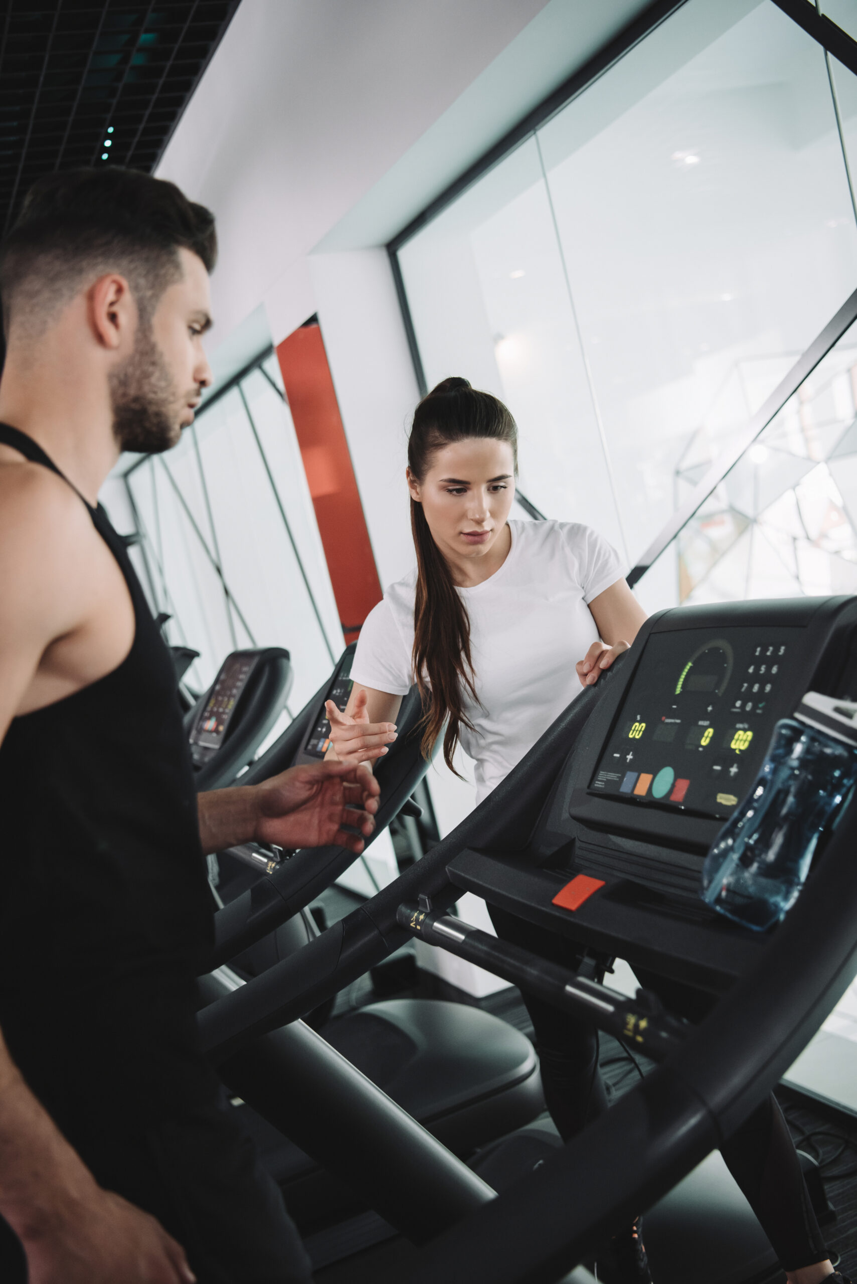 attractive trainer instructing young sportsman standing on treadmill