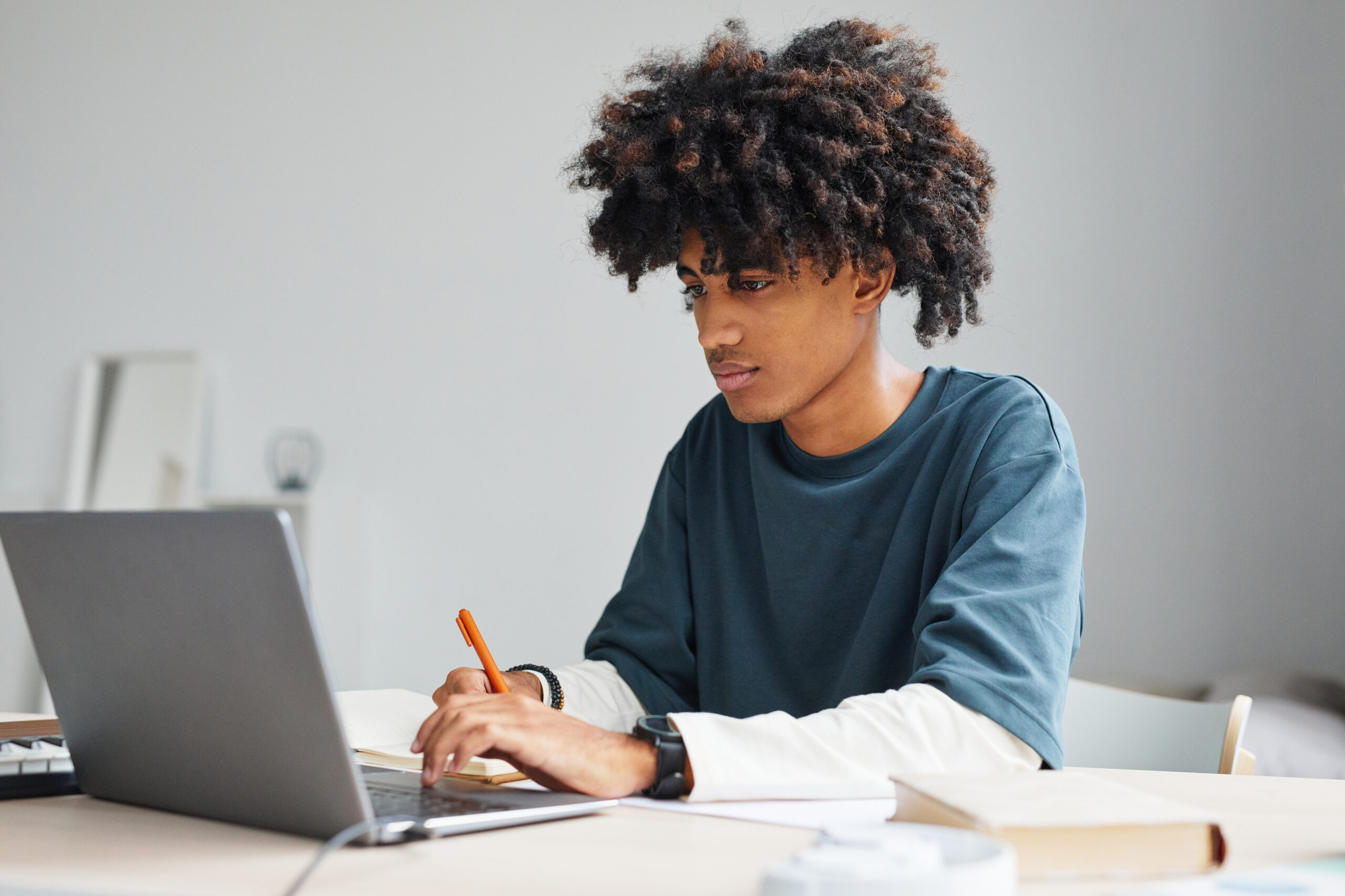 Minimal portrait of African-American teenage boy using laptop while studying at home or in college, copy space
