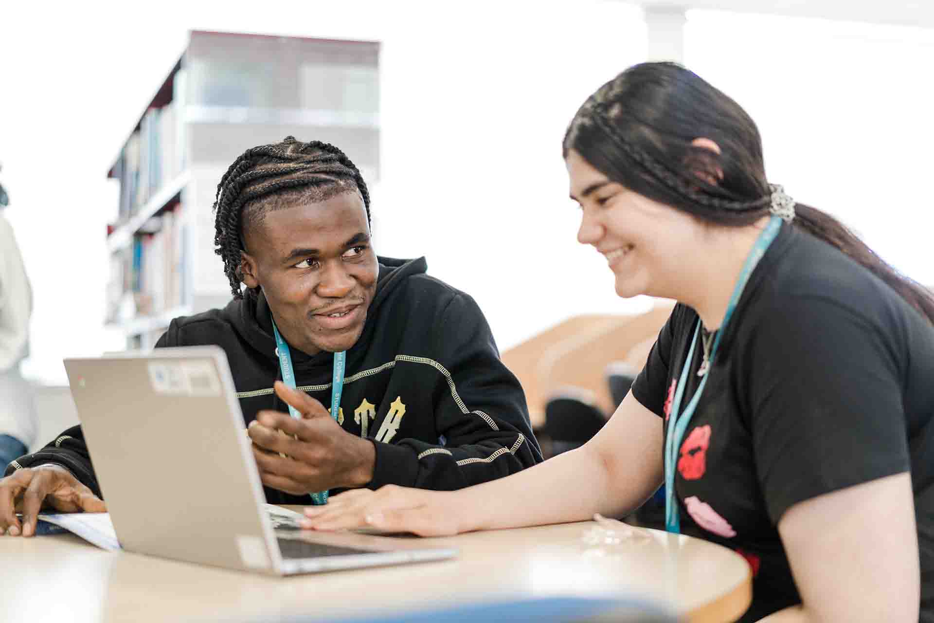 A male student and a female student both in black top wearing Harrogate College lanyard, sitting in front of a laptop having discussion
