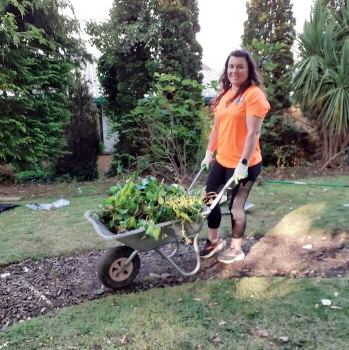 Person smiling whilst pushing a wheelbarrow full of weeds in the Garden of Sanctuary at Harrogate College