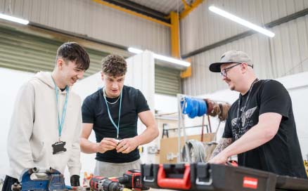 Two students smiling whilst being shown how to use tools in the Harrogate College workshop