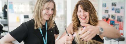 Teacher and student smiling as the teacher shows the student how to cut hair in the hairdressing salon at Harrogate College