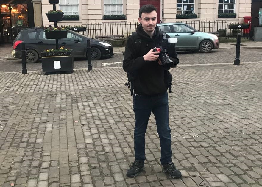 Former Harrogate College student standing in the street holding a DSL camera smiling