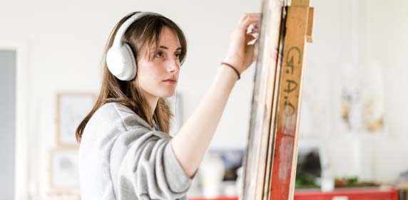 Harrogate College Creative Arts student painting on an easel wearing headphones