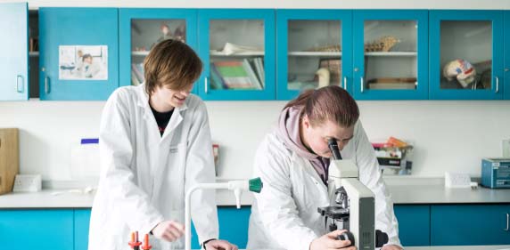 Two students wearing lab coats looking through a microscope