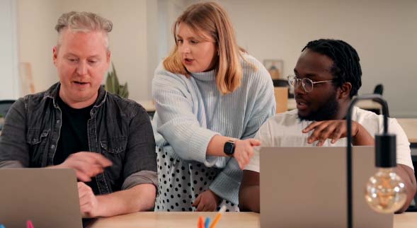 Three people sat around two laptops looking at the screens in discussion