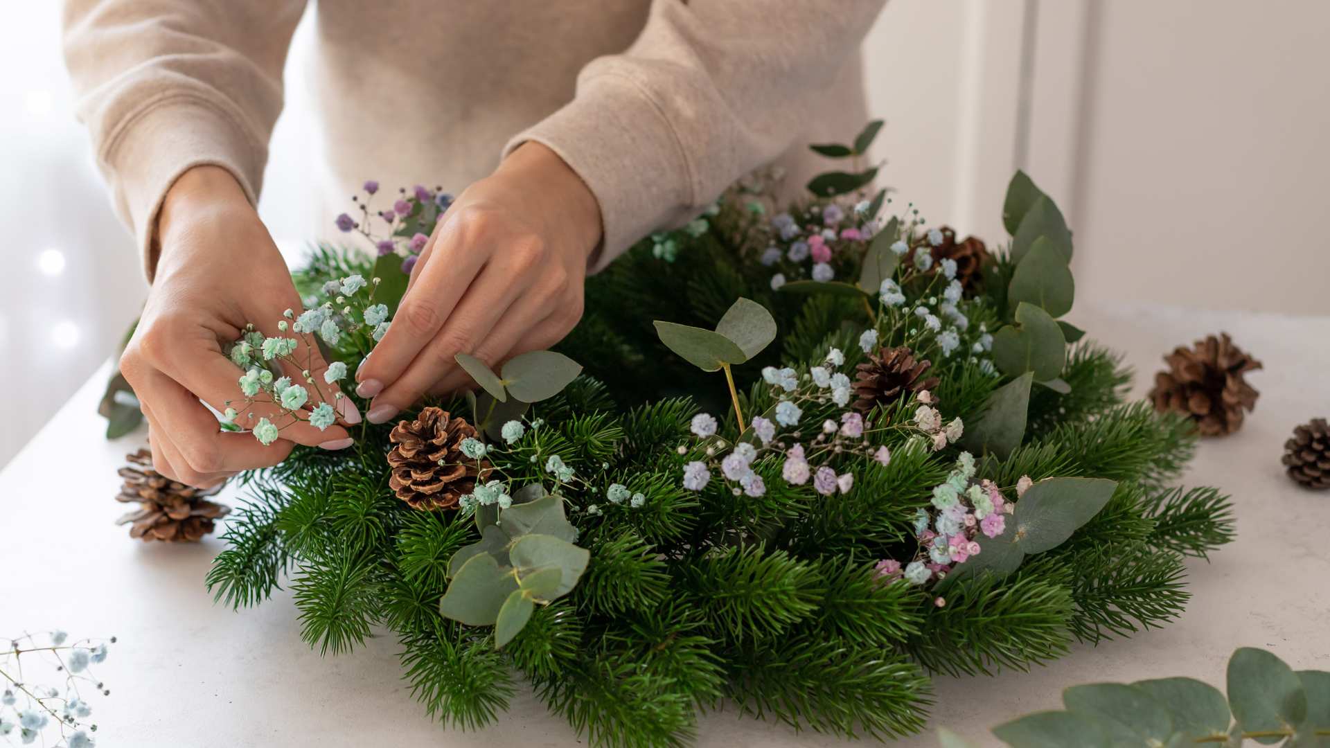A Christmas wreath being made with green shrubbery and flowers with acorns
