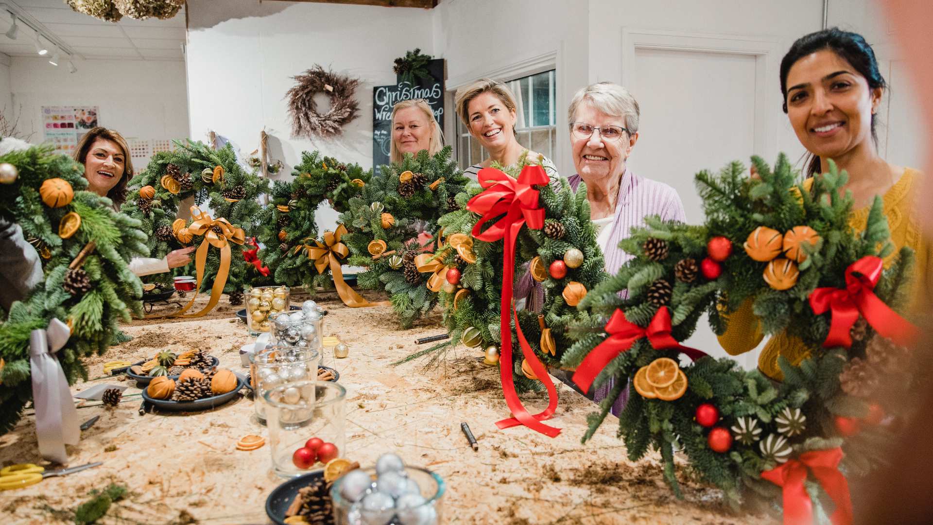 A group photo of attendees to the course displaying Christmas Wreaths they have made