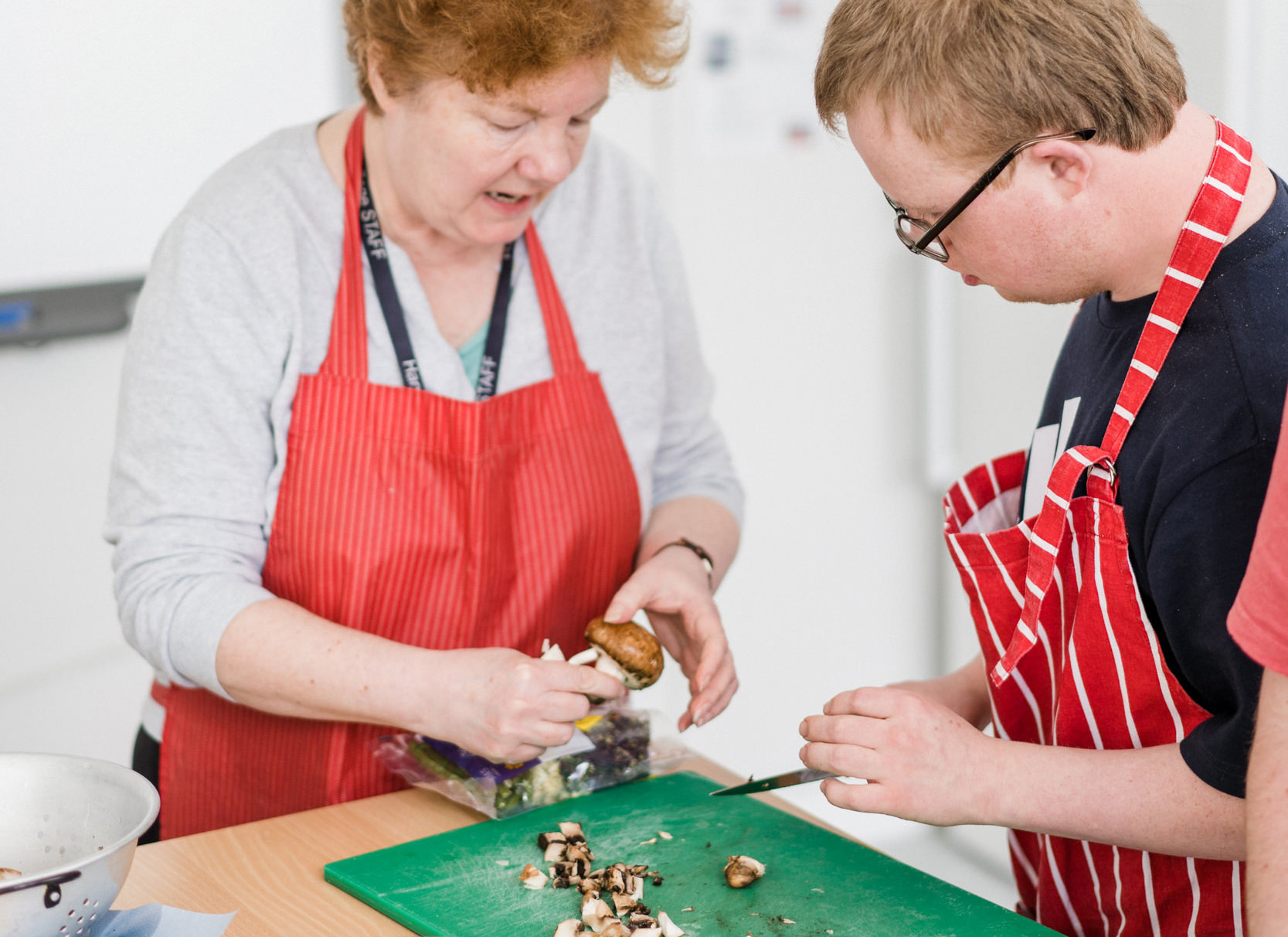 A send support worker is helping a student cutting mushrooms in the kitchen