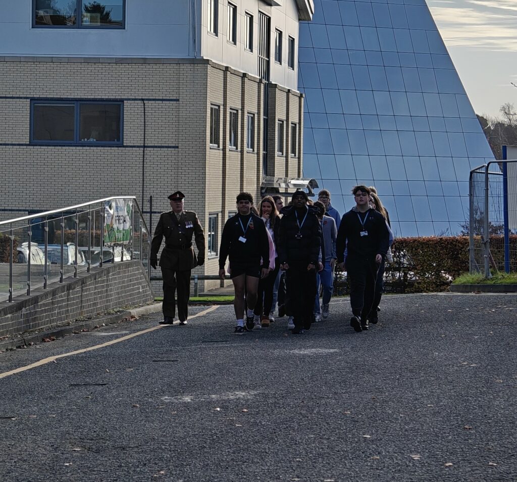 A male soldier marches in a procession with a mix of male and female students