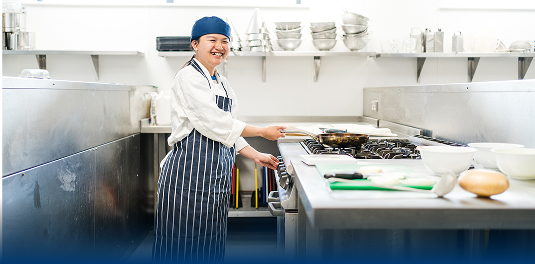 A catering student stood by a frying pan on a stove.
