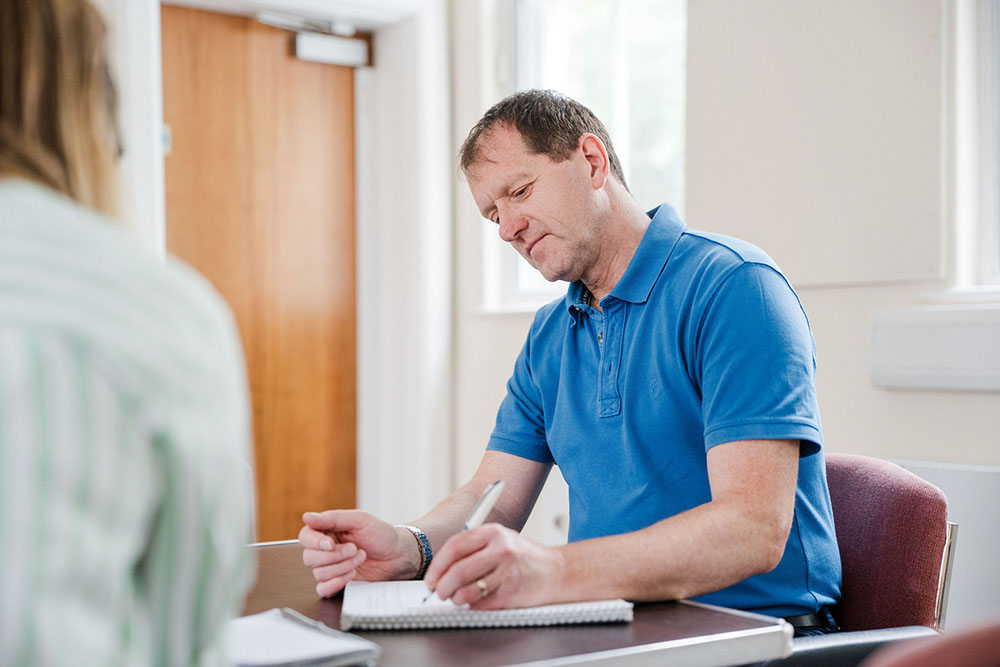 Adult student sat in classroom writing notes in book on desk