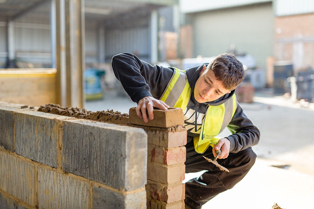 Student in a high vis vest laying a brick on a wall