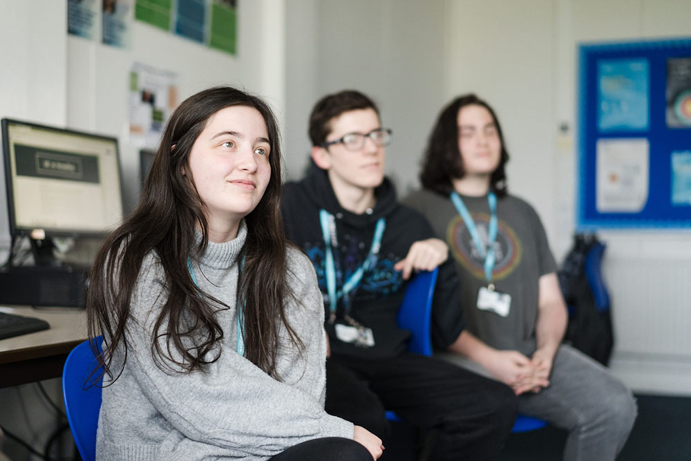 Three students sat in computer room at Harrogate College all looking in the direction of the teacher