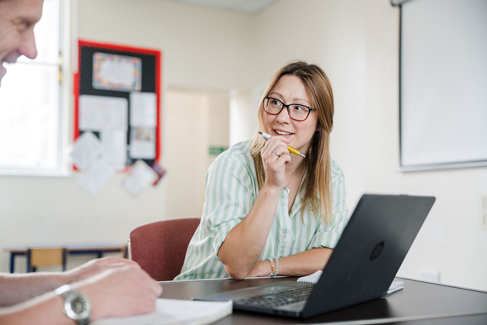 Adult student sat in classroom in front of laptop looking sideways and smiling