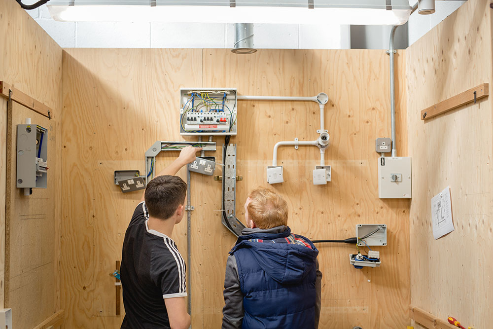 Student and teacher looking at electrical circuits and wiring on the wall in the electrical workshop in Harrogate College