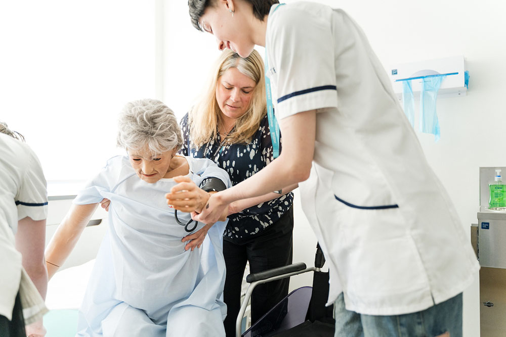 Health student learning how to assist an elderly patient out of their chair