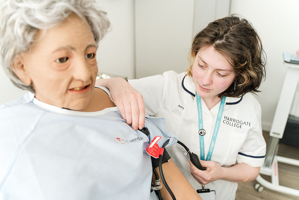 Health student at Harrogate College learning how to take blood pressure - using a medical mannequin for practice