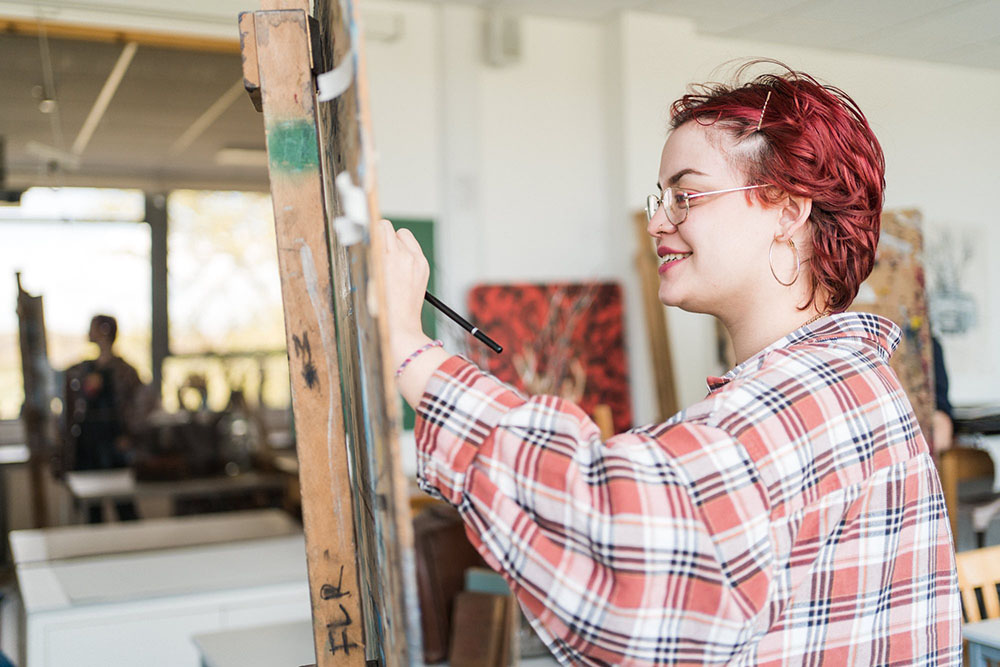 Art student at Harrogate College painting on an easel and smiling