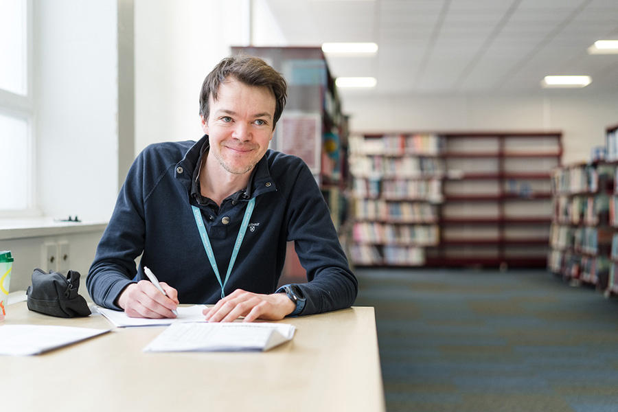 Adult learner sat in library smiling whilst making notes