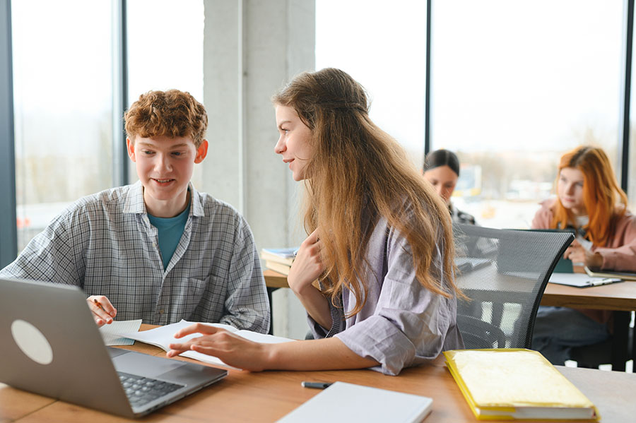 Two students sat in classroom discussing work in front of a laptop