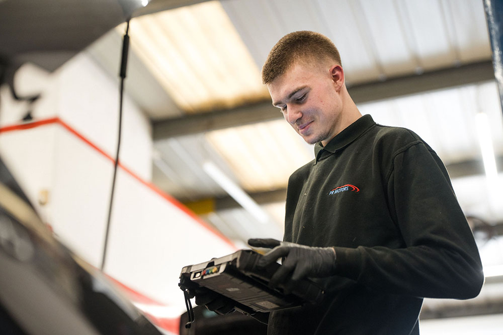 Motor vehicle student looking down and smiling whilst carrying out technical tests