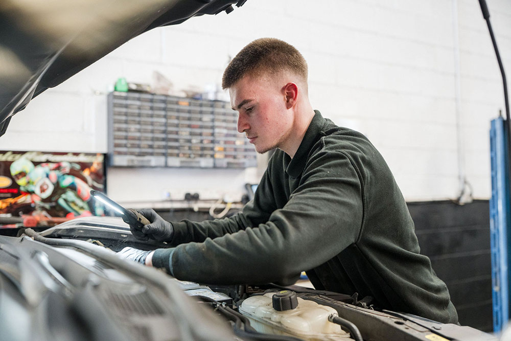 Student checking the engine bay of a car in the motor vehicle workshop