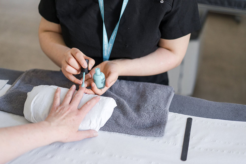 Beauty student at Harrogate College painting someone's nails light blue in the beauty salon