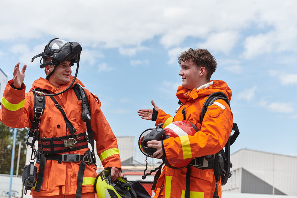 Two firemen in orange firefighter uniform stood outside about to shake hands