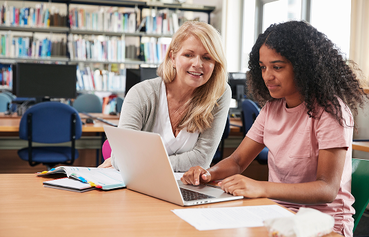 Teacher sitting with student in the library assisting with learning