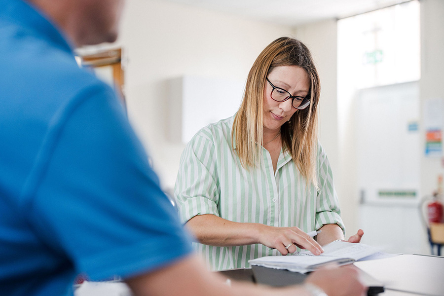 Adult student in classroom sat at a desk looking down at written notes
