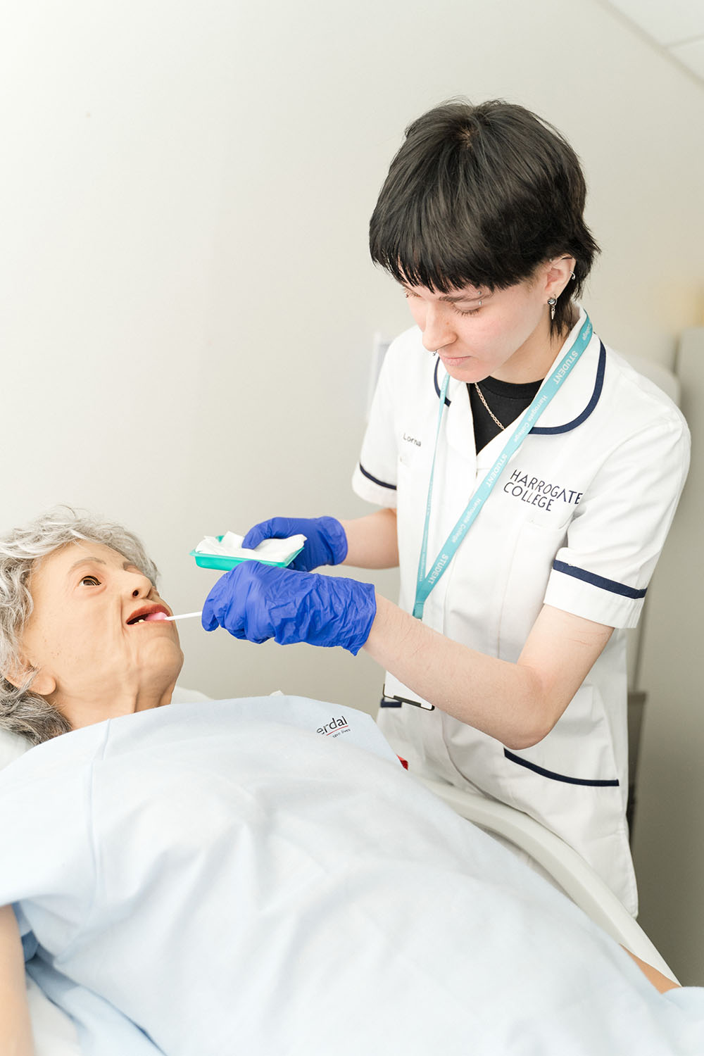 Healthcare student learning to take an elderly person's temperature using a first aid dummy