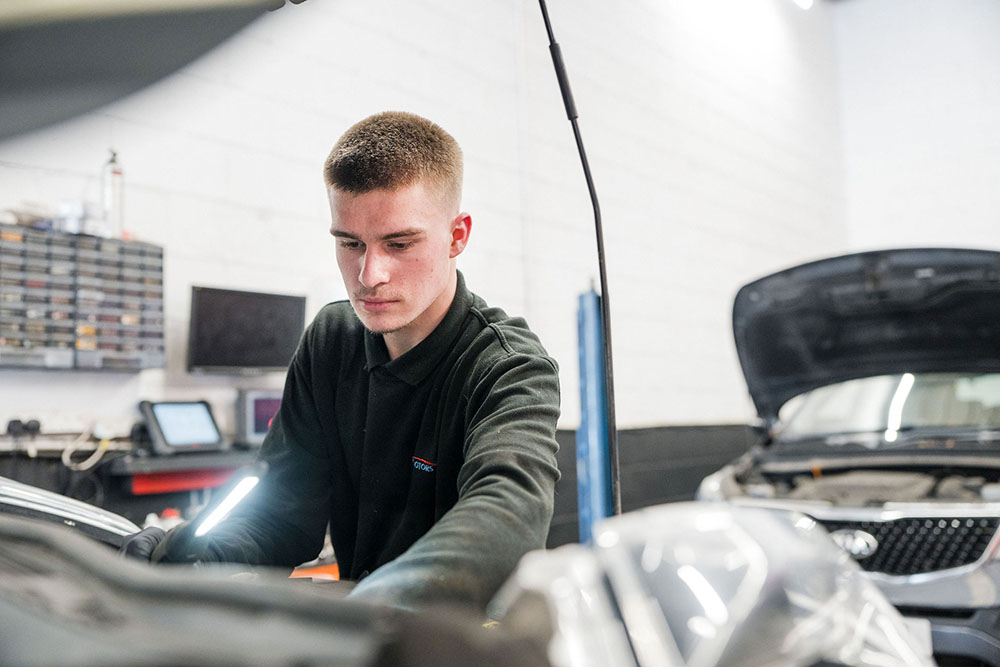 Student checking the engine bay of a car in the motor vehicle workshop