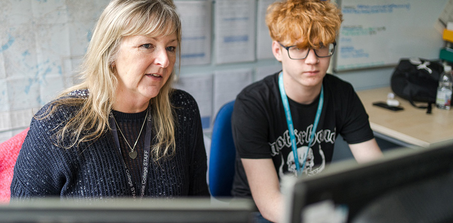 Harrogate College teacher and student sat at desk in classroom looking at computer screens together