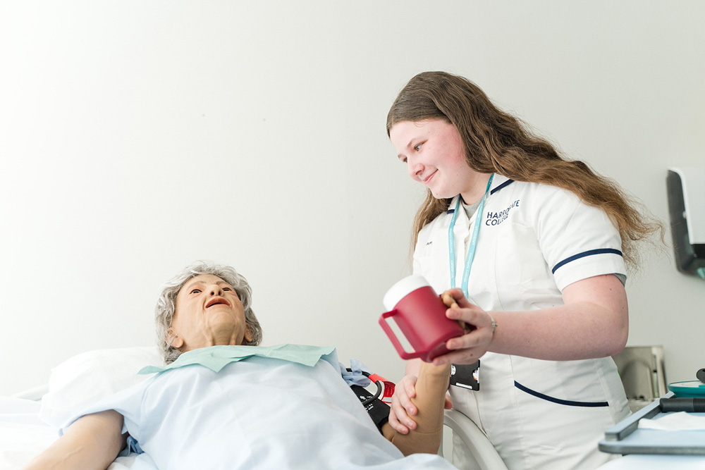 Health student practising assisting a first aid mannequin dummy with a drink of water