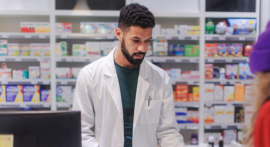 Pharmacist stood behind counter wearing medical uniform
