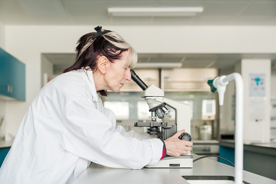 Adult student in lab coat looking through microscope in Science classroom at Harrogate College