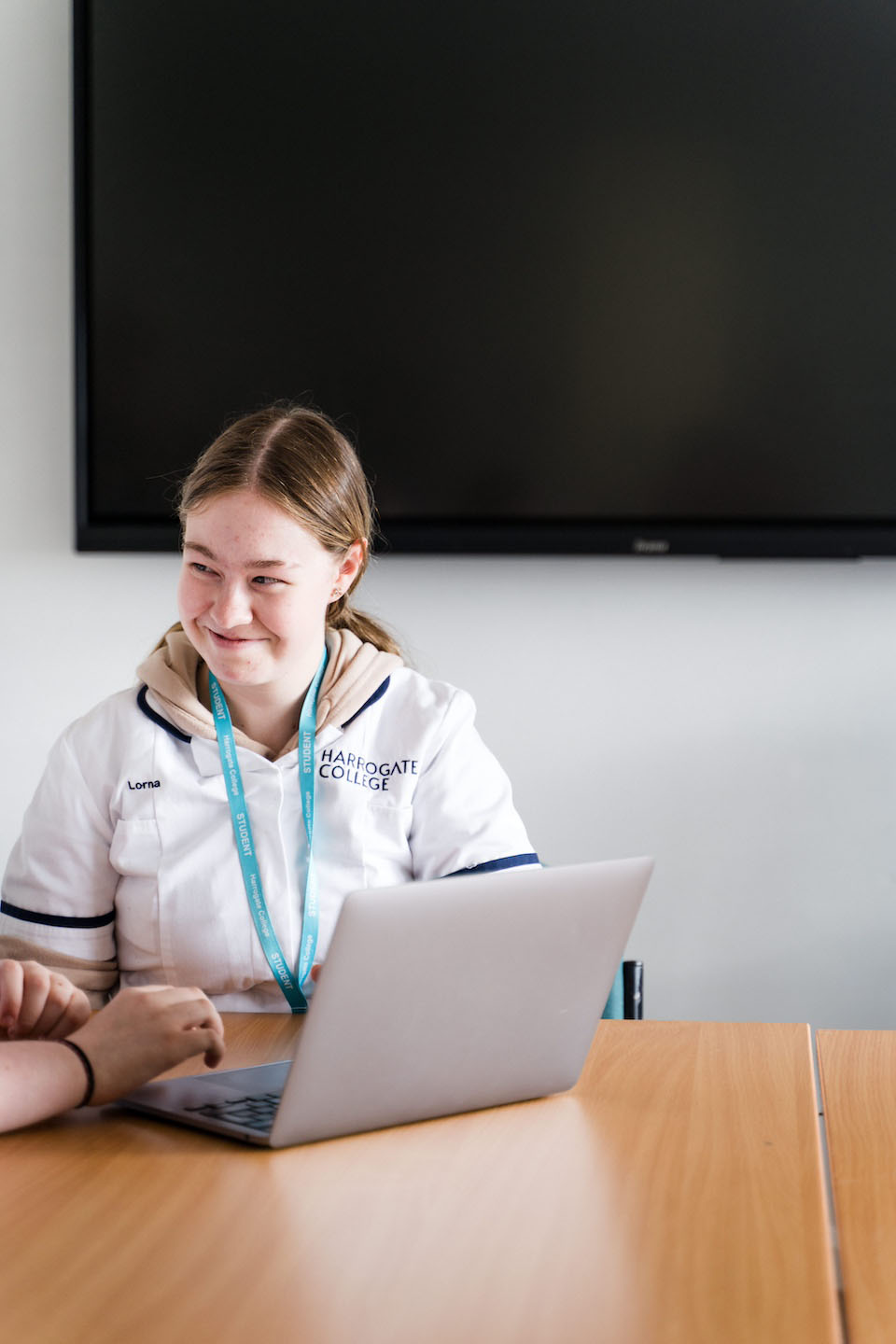 Student smiling sat at laptop wearing healthcare uniform and lanyard
