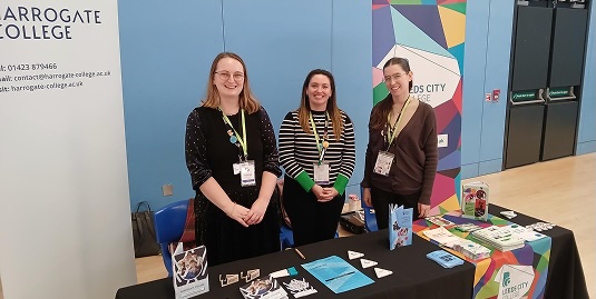 Three teachers stood behind their kiosk at an event smiling
