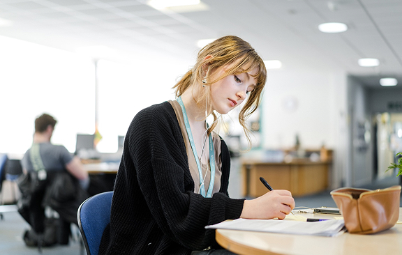 Student sitting in the main entrance study area writing notes