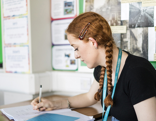 Harrogate College student sitting at a desk in a classroom writing down notes