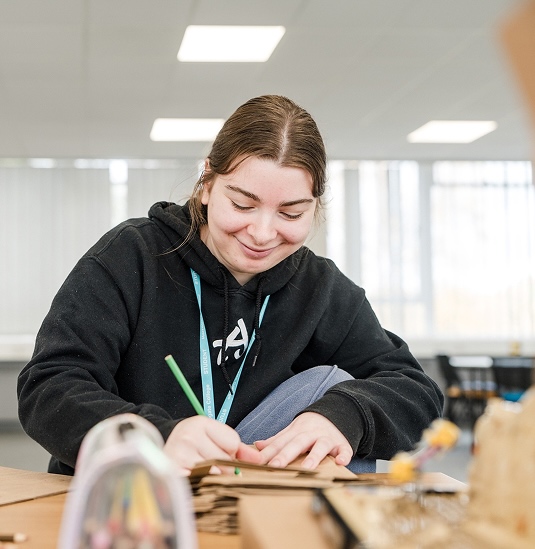 Harrogate College studnt sat at a table smiling while writing
