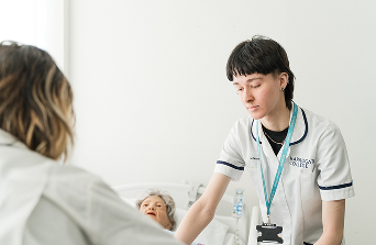 Health care student practising looking after an elderly patient lying down in care home bed