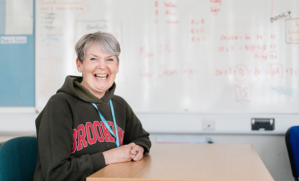 Adult student sat at desk in classroom smiling at camera