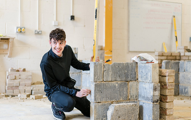Student in the brickwork workshop measuring wall and smiling