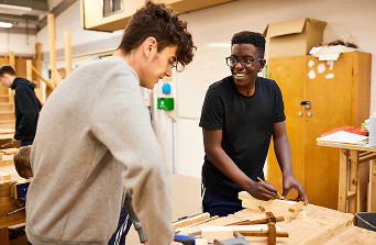 Two students in wood workshop looking down measuring wood