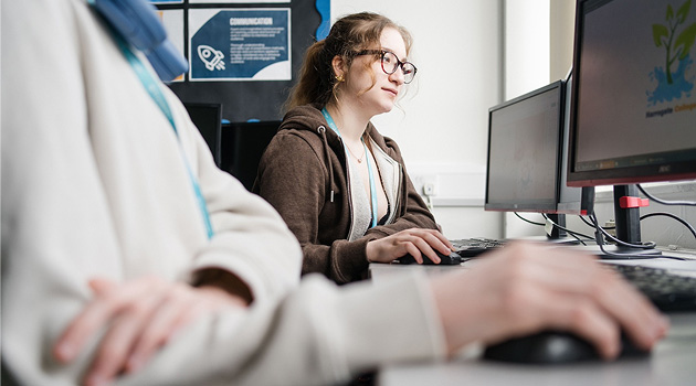 Student sat at a desktop computer looking at the screen, hand on mouse