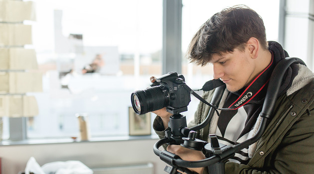 Student holding camera equipment looking through camera lens taking a photo
