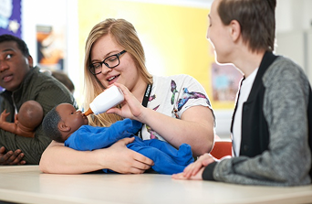 Early years students learning how to hold and feed a baby a milk bottle by using baby training dolls
