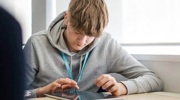 Student sat at a desk looking down and working on ipad screen